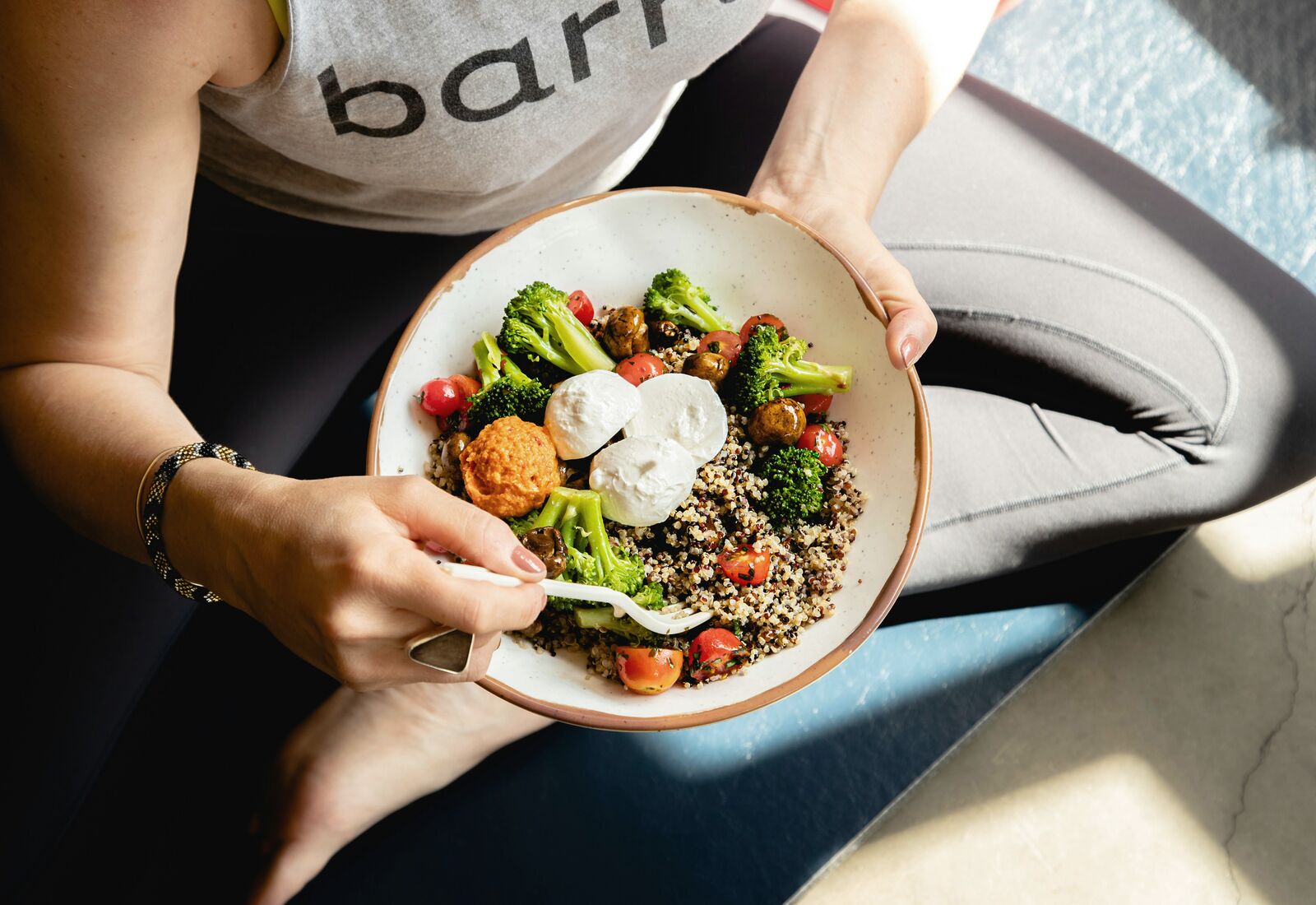 A bowl of grains, broccoli and tomatoes held in two hands